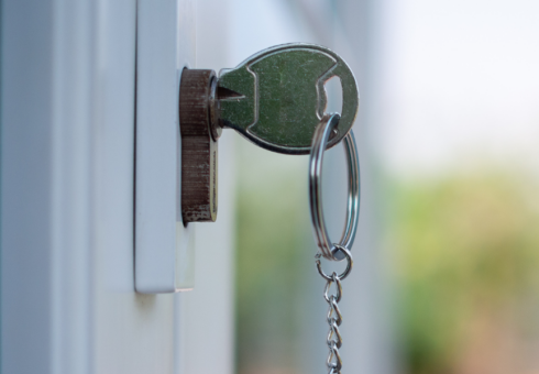 photo showing a key in the lock of a door to a home; the key is on a keychain with a small wooden house charm
