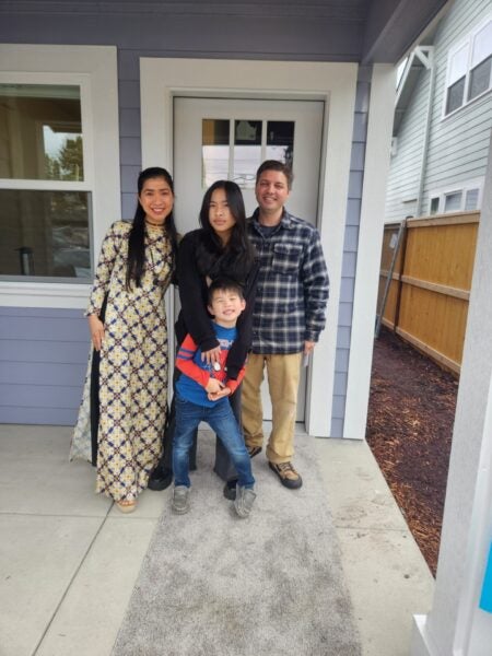 Thi and Jerard pose with their children in front of the front door of their finished home.